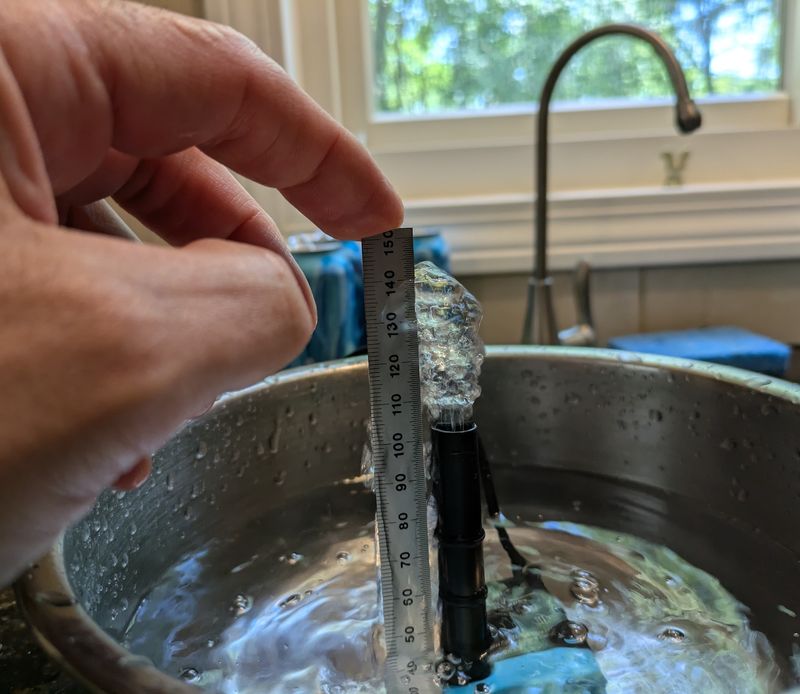 A steel rule held beside the pump's outlet in a bowl of water, measuring how high the water rises in order to estimate the pump's head pressure.