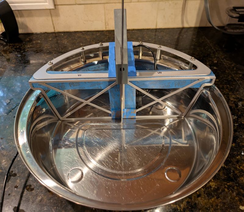 Front view of the 3D-printed test parts held in the stainless bowl with blue painter's tape, showing how the top frame and its cross braces rest on the rim.