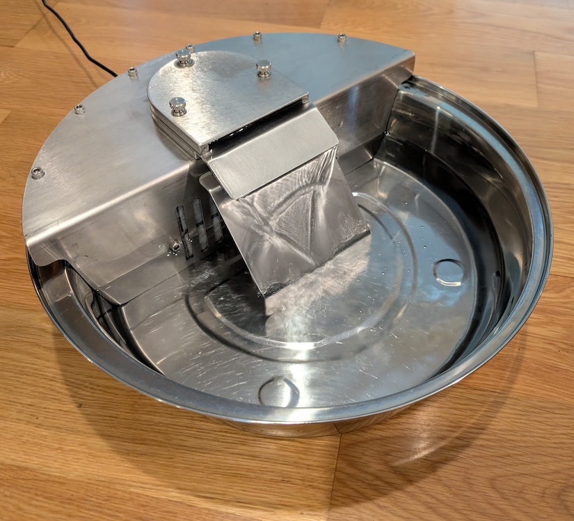 The finished stainless steel bowl on a wood floor, with water running down the sloped spillway into the pool below.